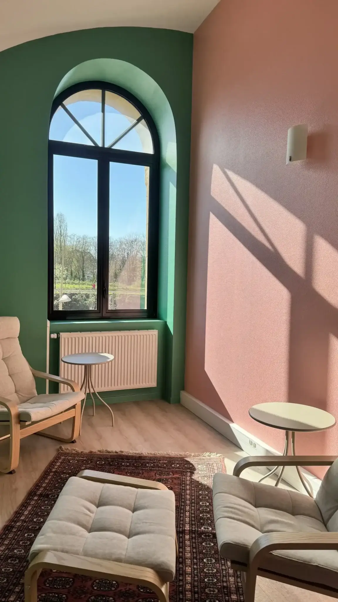 Le cabinet de sophrologie à Metz : deux fauteuils, un tapis et une grande fenêtre en arc ouverte sur la verdure